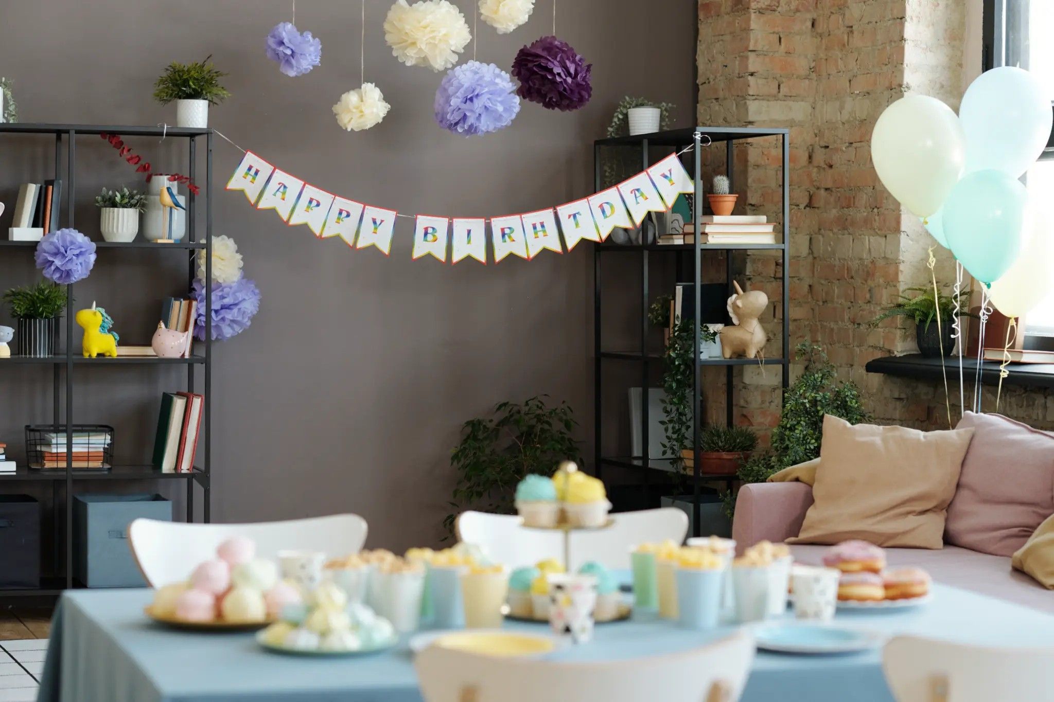 Pastel birthday decorations with paper flowers, balloons and a Happy Birthday banner over a dessert table