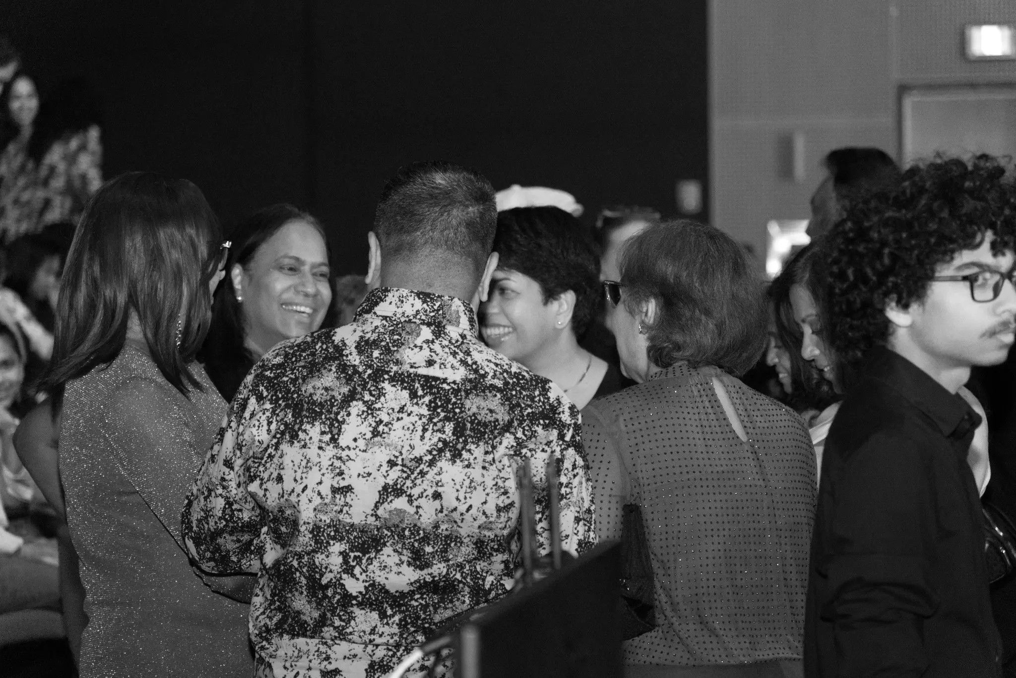 Black and white candid of guests laughing and mingling at a birthday celebration